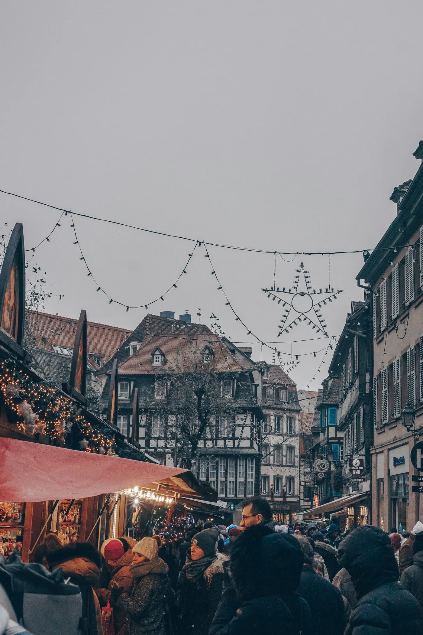 Illuminated Alsace Christmas market with wooden stalls, string lights and half-timbered houses