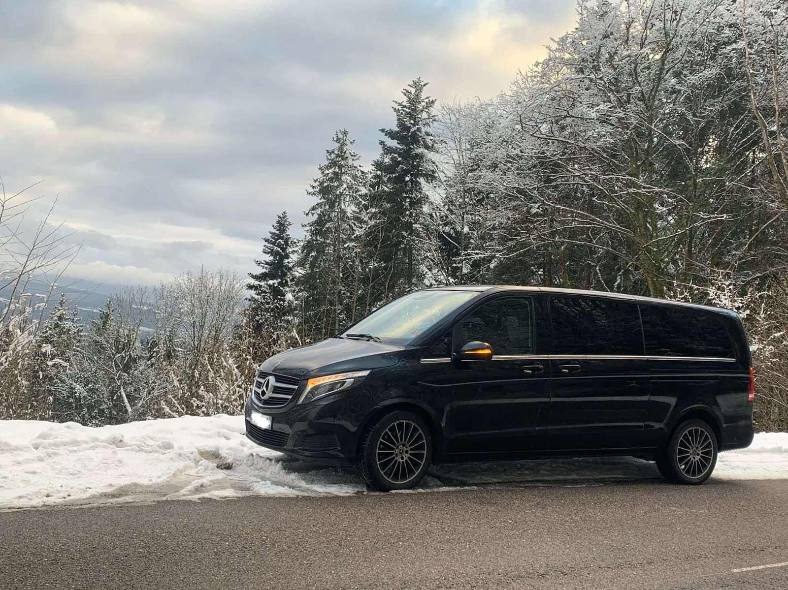 Black Mercedes V-Class 8-seater van on a snowy Alsace road in winter — private Christmas market driver from Strasbourg